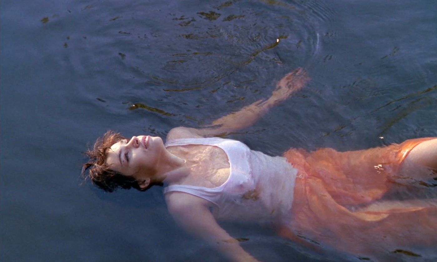 A woman, clothed, floating in a river looking up.