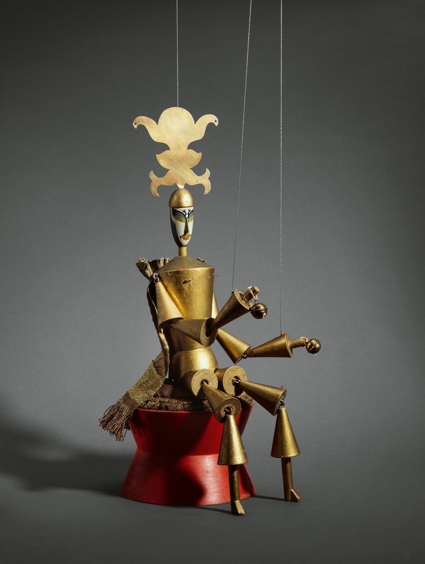 A marionette of a king, painted all gold, except for his white face. The crown is a strange organic shape, not resembling a real crown, and his arms and legs are formed of cones.